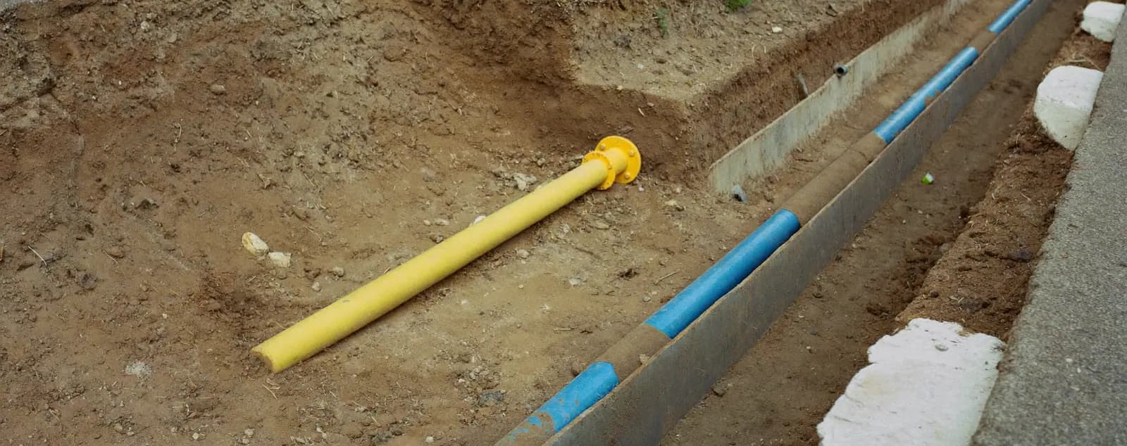 Scavo con una tubazione gialla del gas e una blu dell’acqua affiancate.